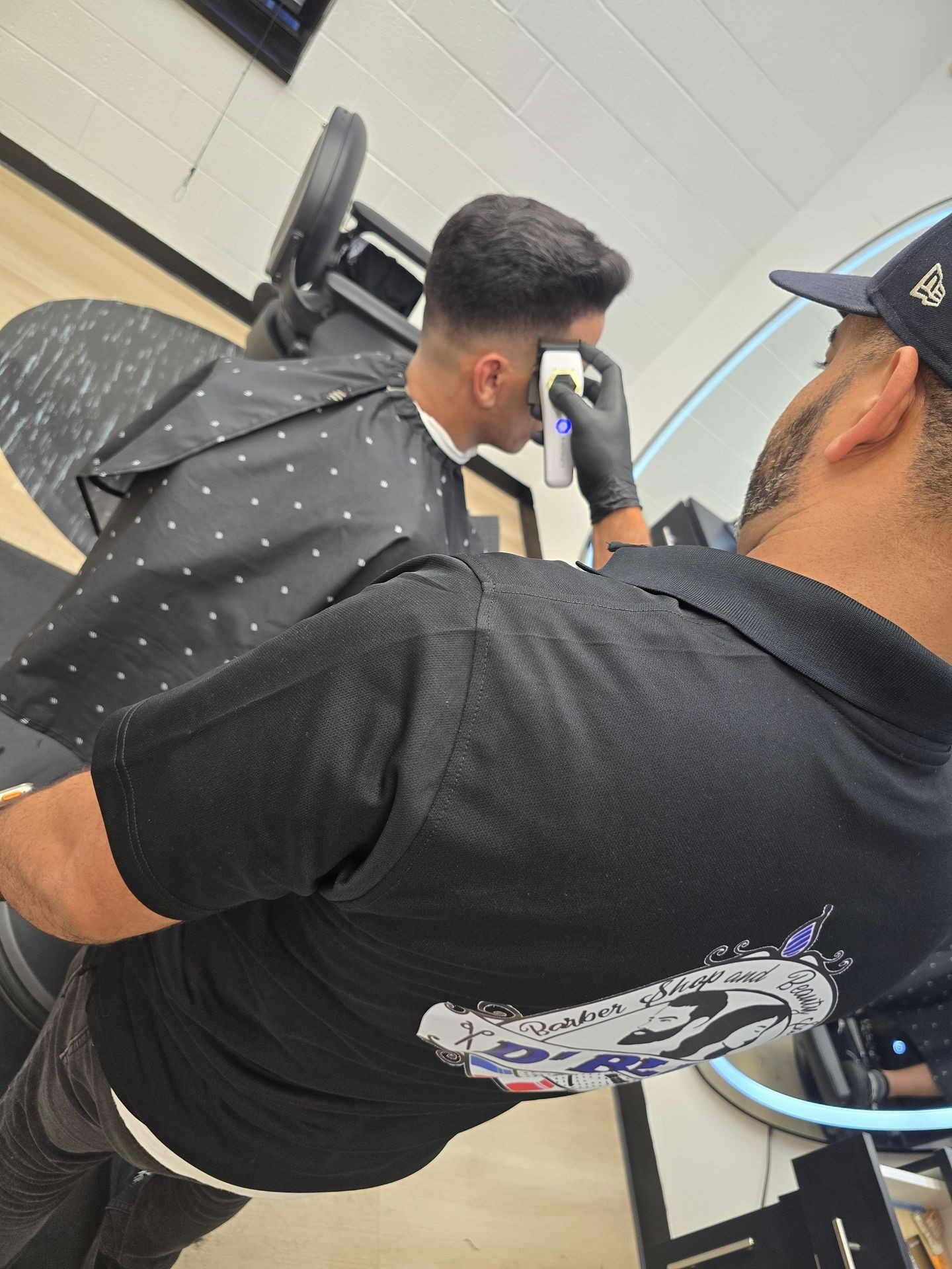 Barber giving a haircut with clippers to a seated client in a modern barber shop.